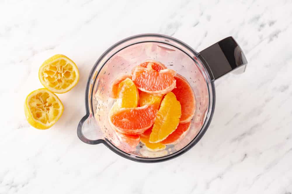 Ingredients for a smoothie in a blender with lemon halves on the side.