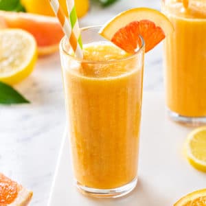 Citrus smoothie in a glass with an orange wedge on the rim and two straws.