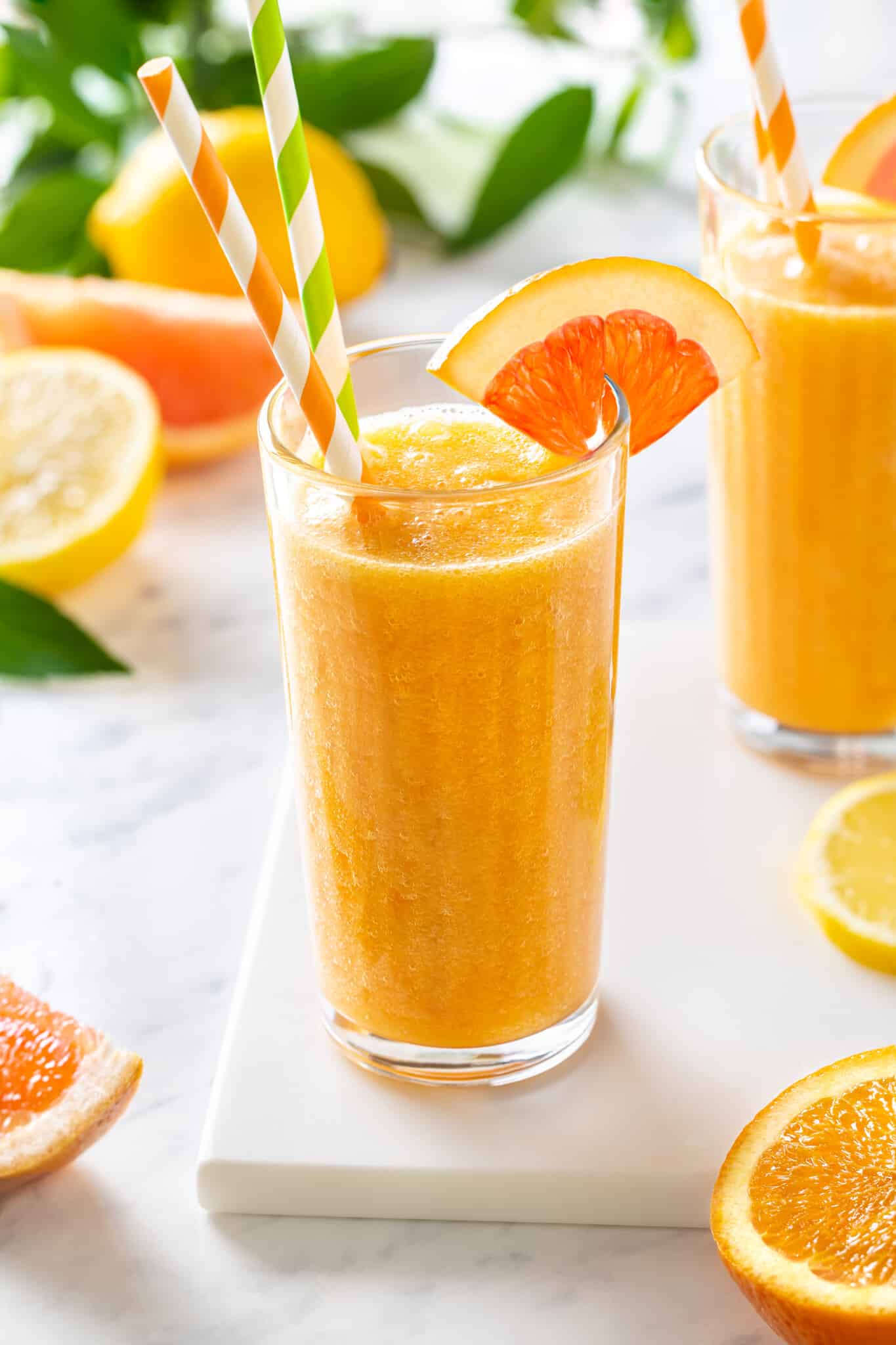 Citrus smoothie in a glass with an orange wedge on the rim and two straws.