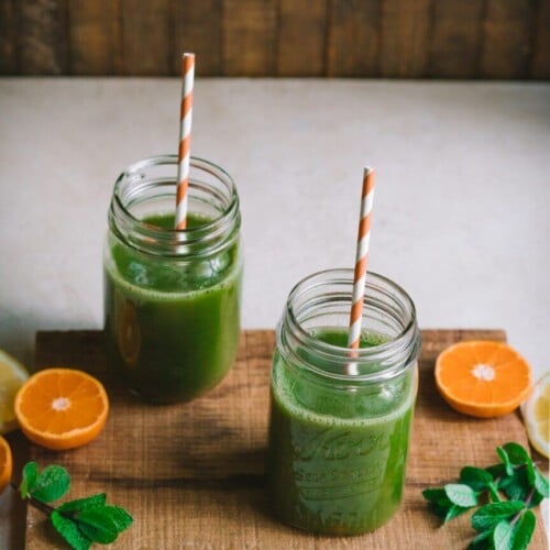 citrus-smoothie-in-glass-jars-with-straws-on-a-wooden-board-with-oranges-and-mint-on-the-board