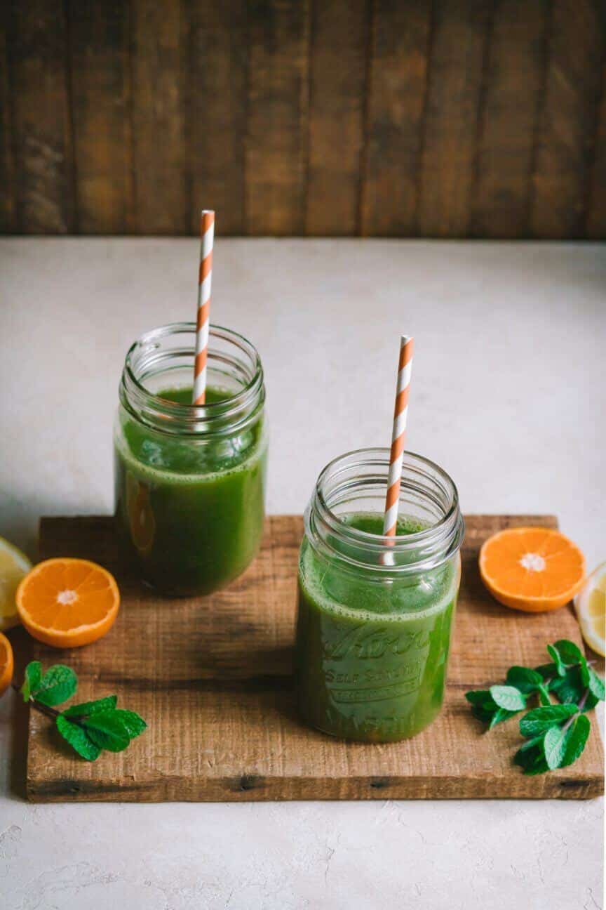 citrus-smoothie-in-glass-jars-with-straws-on-a-wooden-board-with-oranges-and-mint-on-the-board