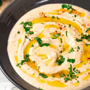 Close up of hummus in a bowl with olive oil and parsley.