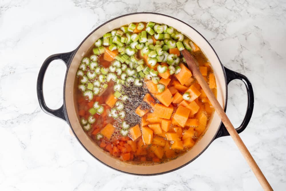 Vegetables cooking in broth in a large pot, mixing with a wooden spoon.