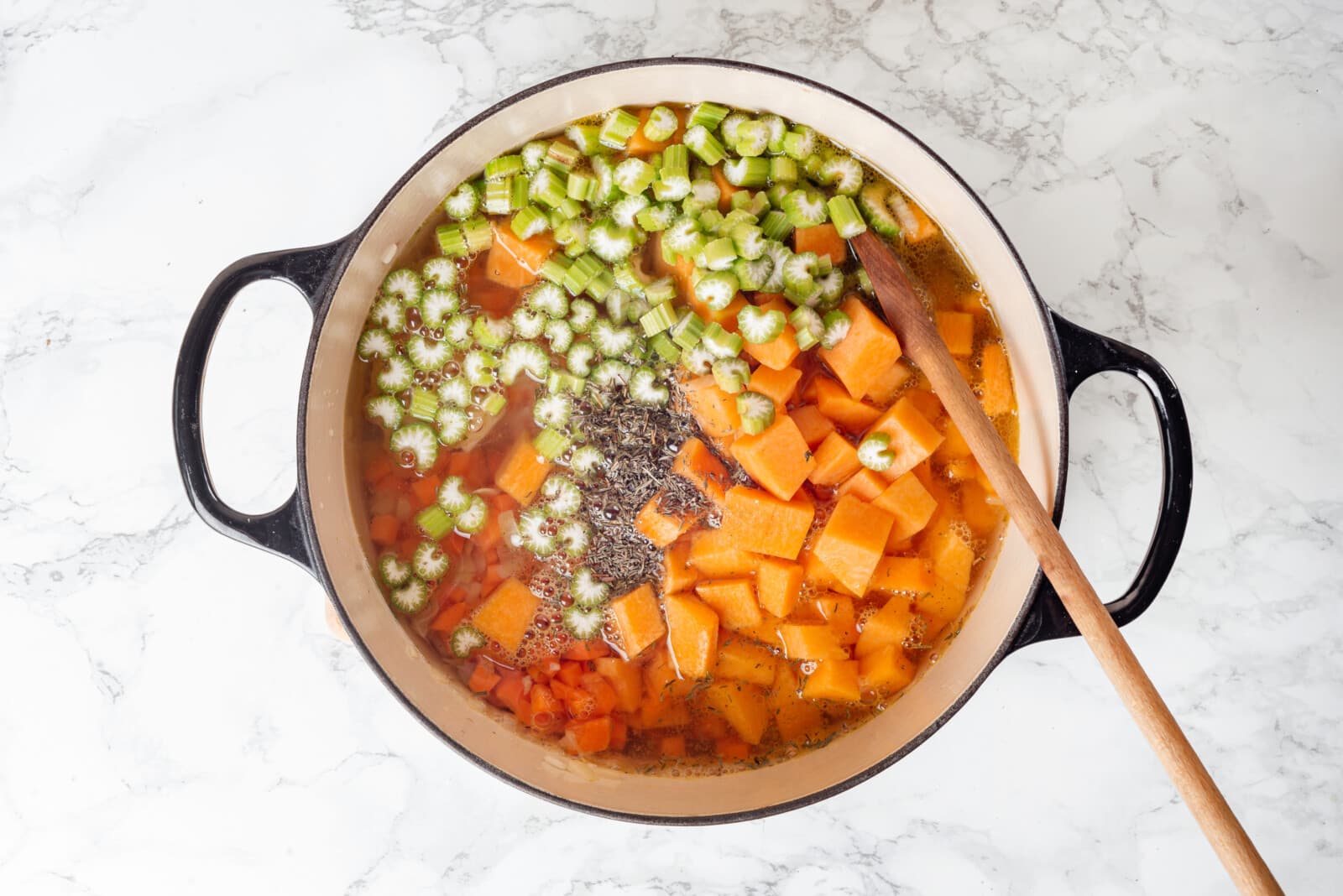 Vegetables cooking in broth in a large pot, mixing with a wooden spoon.