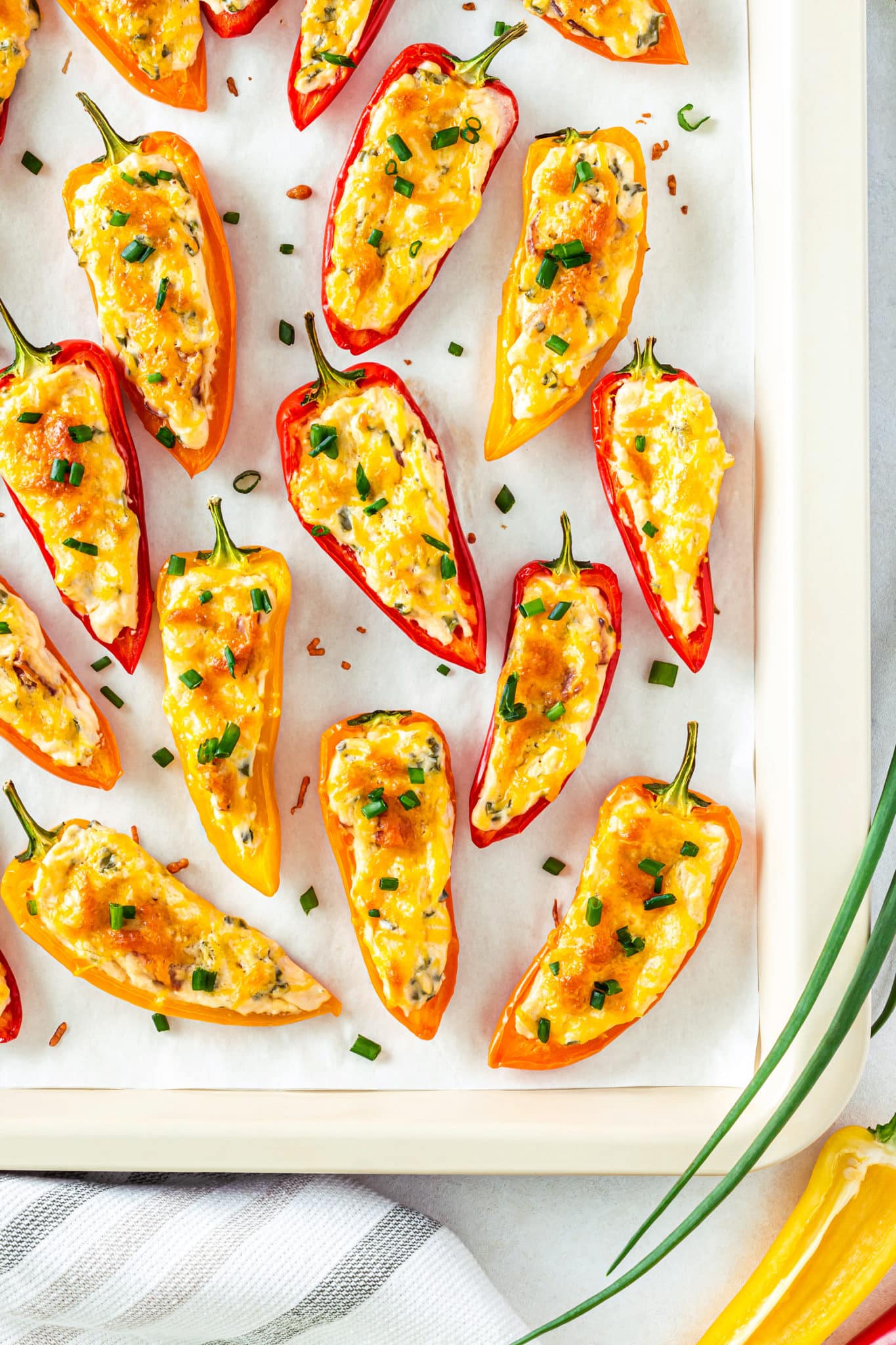 Cream cheese filled bell peppers with green onion on top on a baking tray.