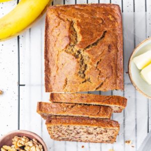 sliced banana bread on a wire rack with a banana butter and walnuts in three bowls on the side.