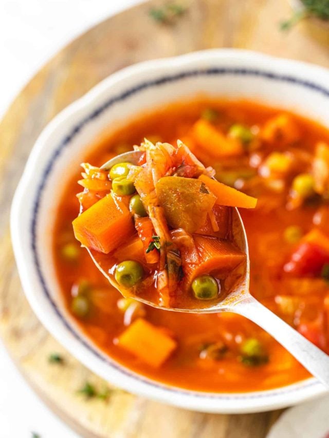 a vegetable soup on a spoon and in a bowl on a wooden board.