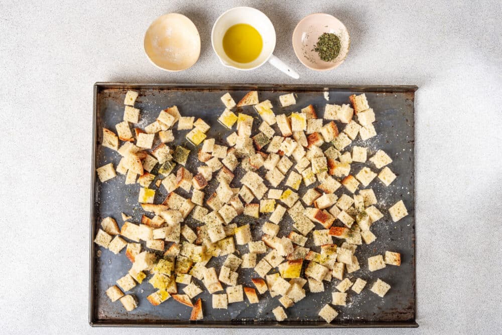 Bread on a baking tray with seasonings and olive oil on the side.