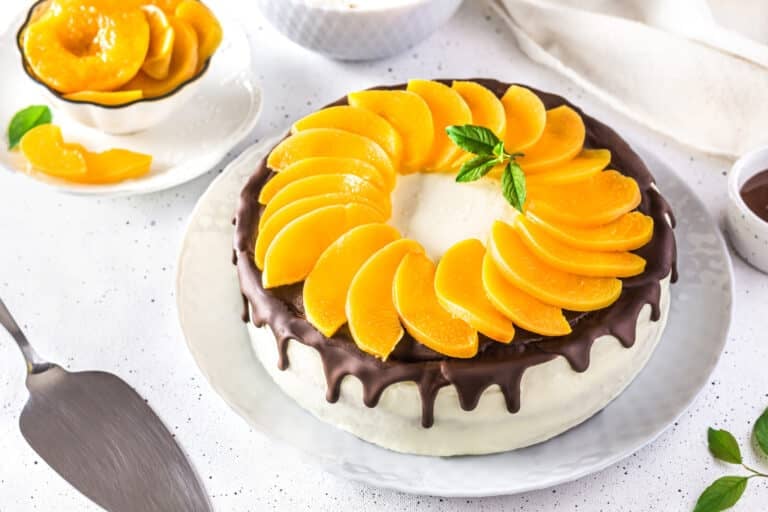 Decorated peach mousse cake with peach slices on a white plate.