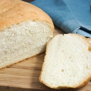 bread-on-a-wooden-board-with-slices-a-knife-and-a-blue-towel