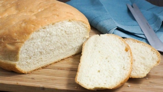 bread-on-a-wooden-board-with-slices-a-knife-and-a-blue-towel