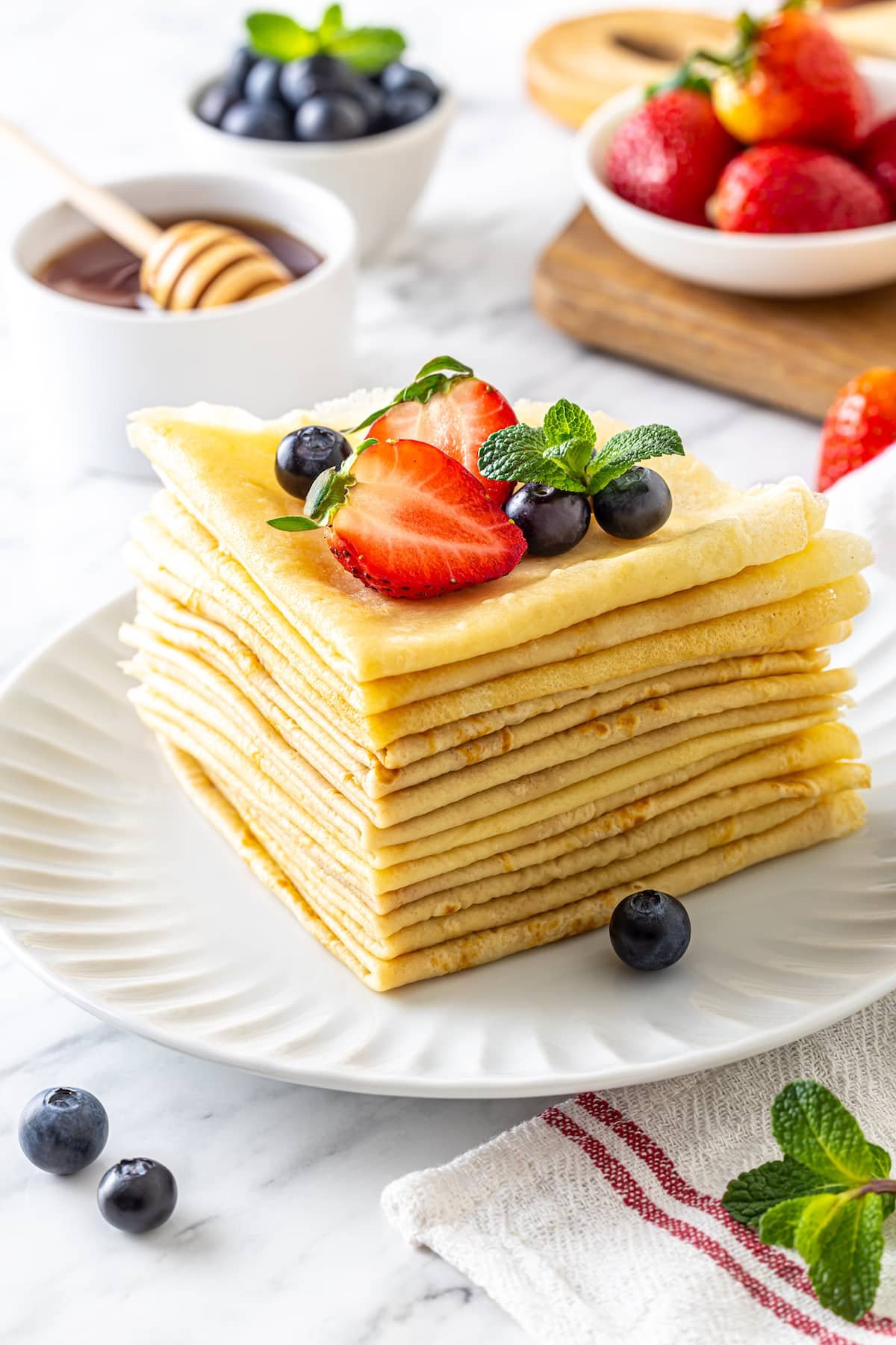 A stack of folded crepes with berries on top and more on the side.