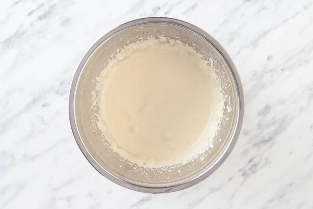 Egg yolks and sugar mixed in a silver mixer bowl.