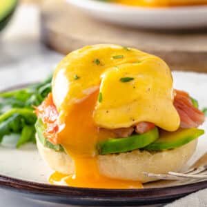 smoked salmon eggs benedict with the poached egg leaking yolk onto the white plate