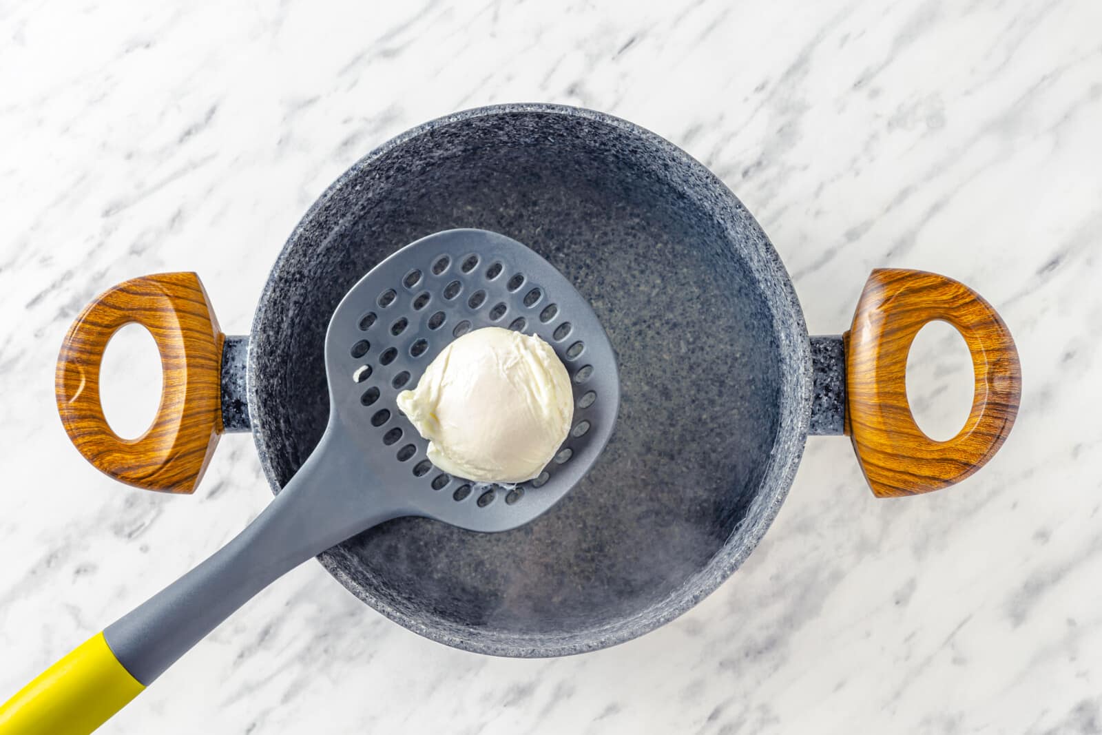 a slotted spoon holding a poached egg over a pot of boiling water