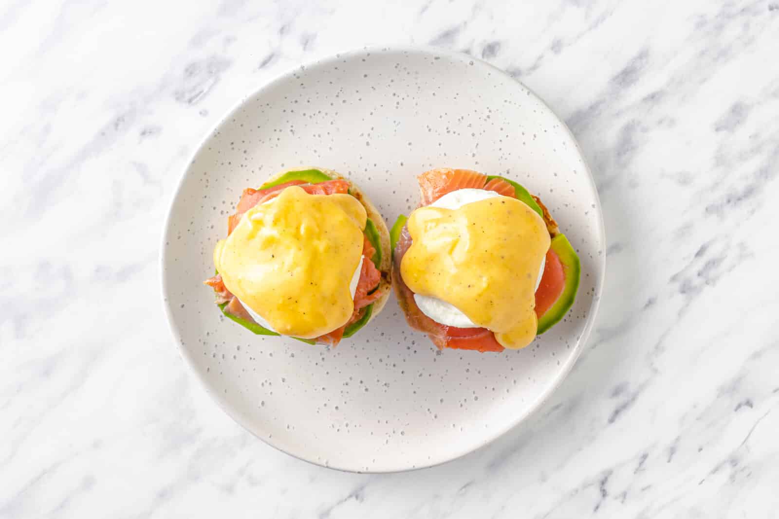 hollandaise sauce on top of smoked salmon eggs benedict on a white plate