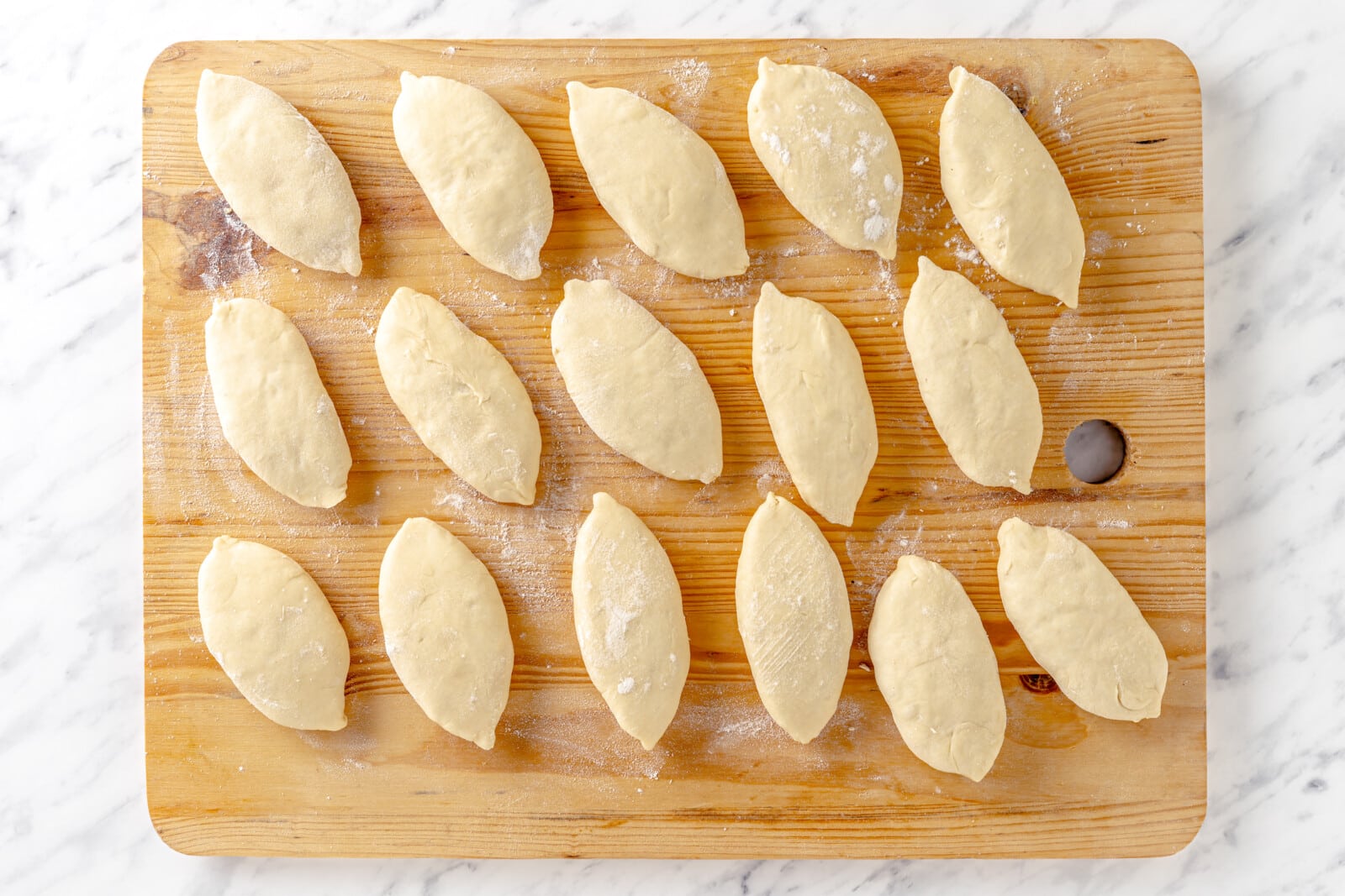 Filled and closed raw piroshki on a wooden board.