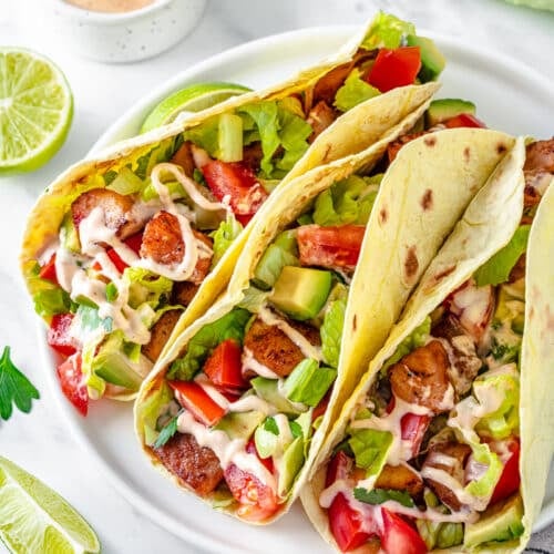 tacos with veggies and seafood filling on a white plate.