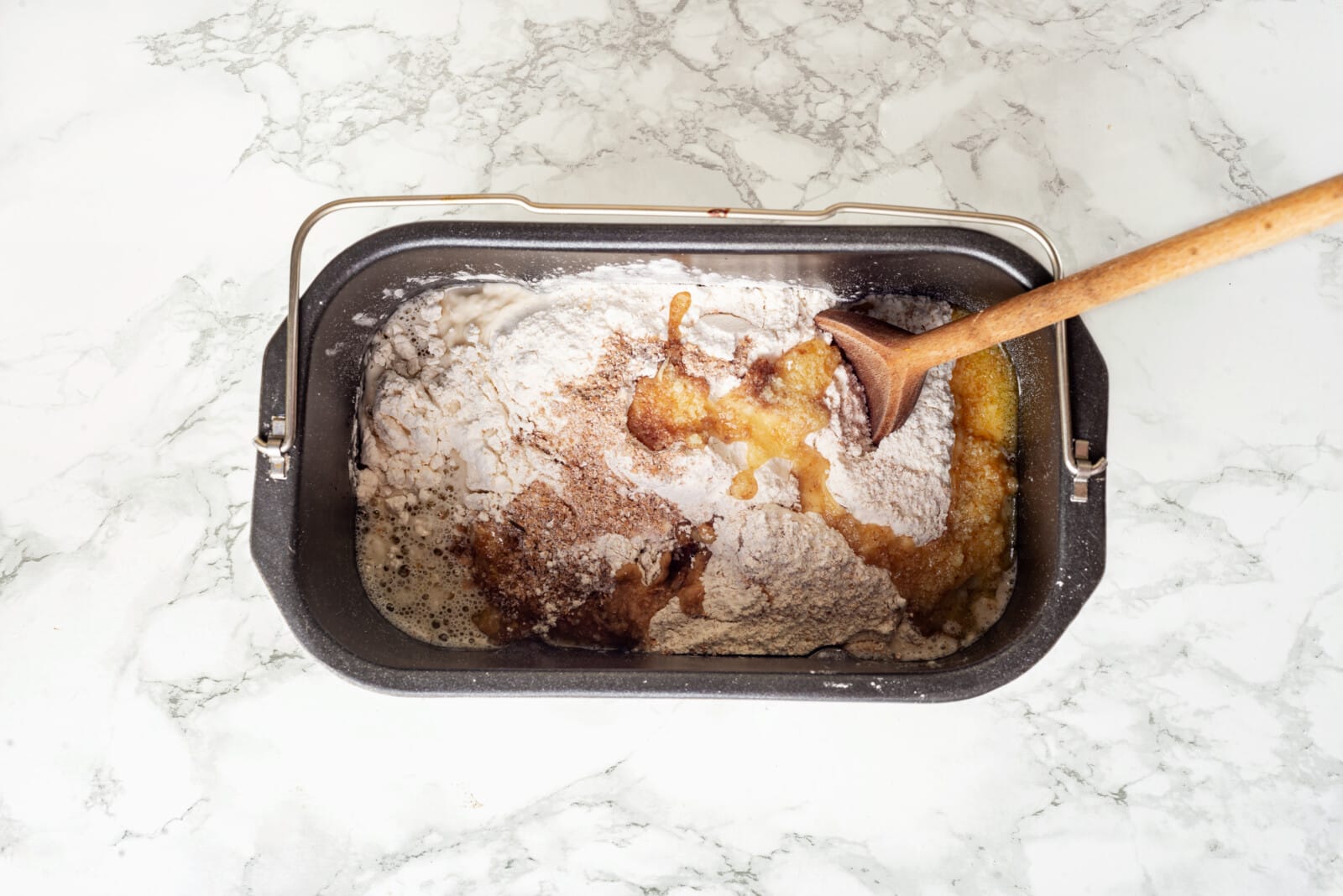 Flour added to ingredients mixing with a wooden spoon.