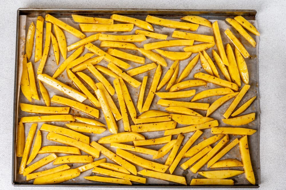 Fries ready to bake on a baking sheet, seasoned.