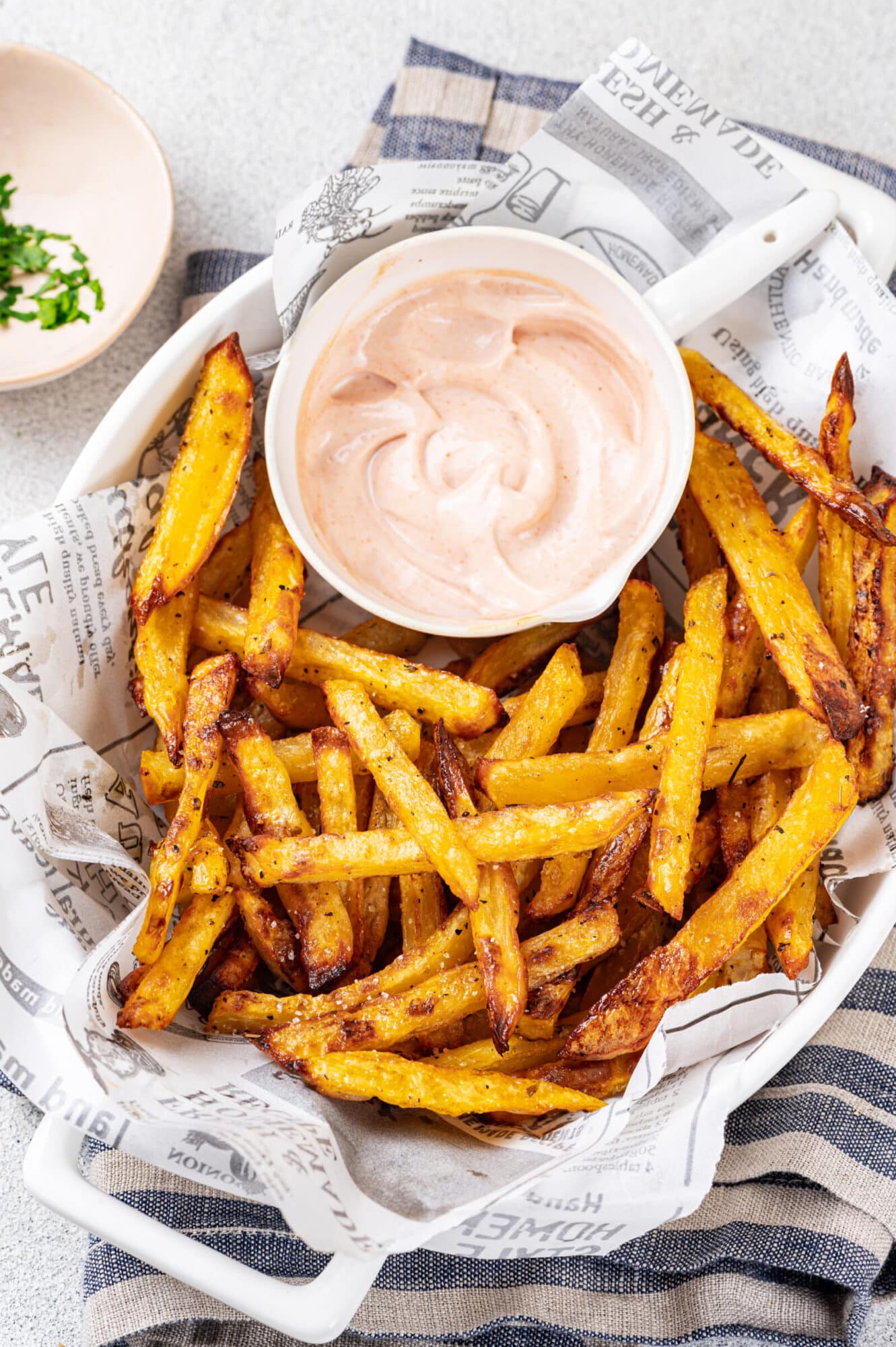 Fries served in a basket with paper and a sauce on the side.