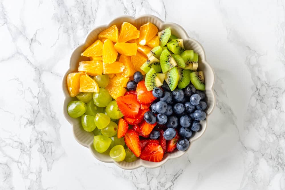 white bowl with orange slices, sliced kiwi, blueberry, sliced strawberries, and sliced grapes.