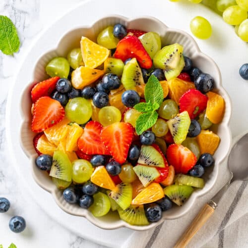 bowl of fruit mixed together in a white bowl on a white background with a tablespoon on the side.