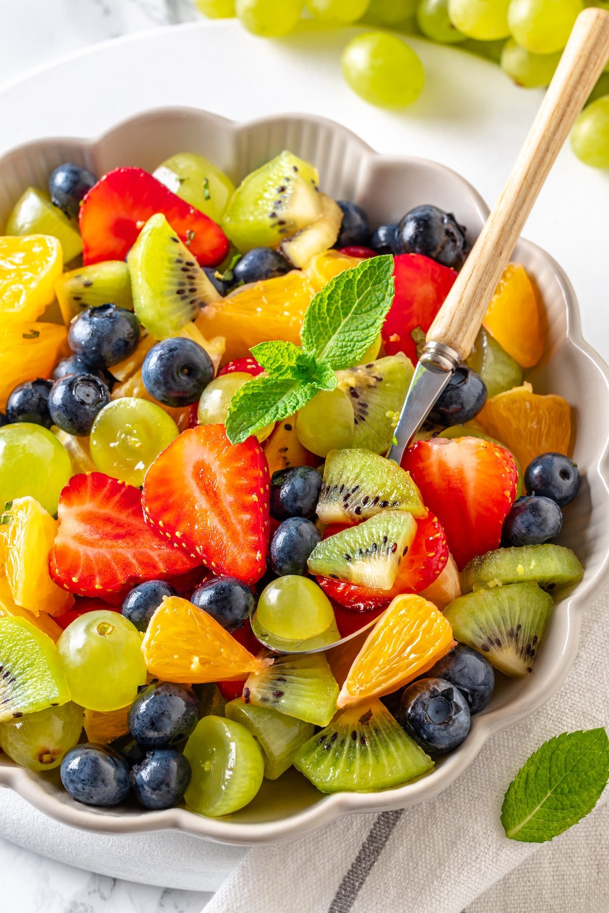 a white bowl of fruit salad with a wooden handle spoon on white background.
