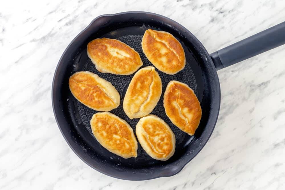 Frying piroshki on a black skillet.