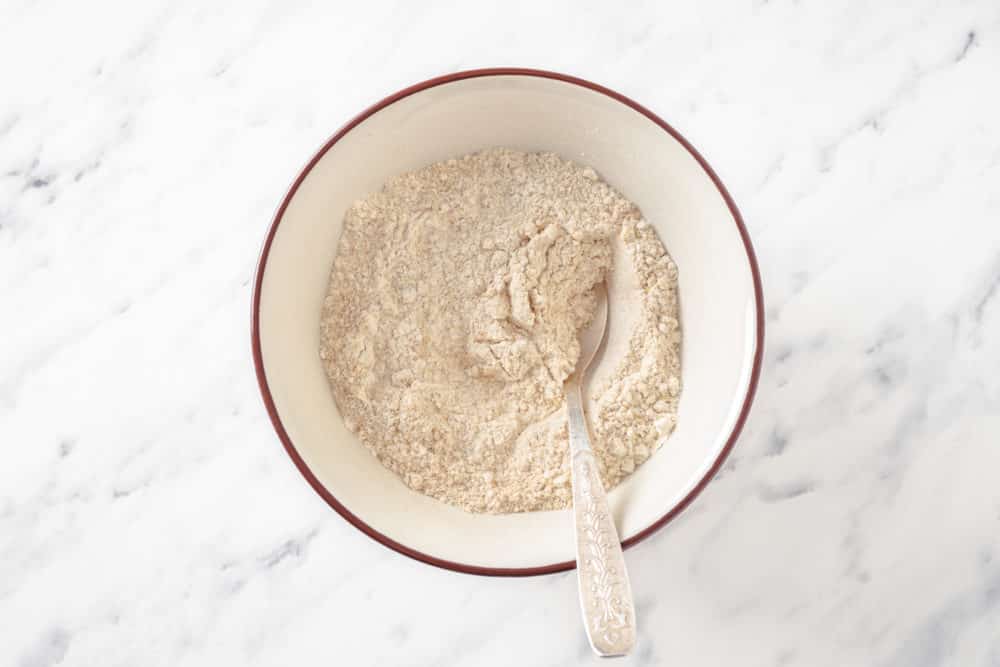 flour in a white bowl with a spoon in the bowl.