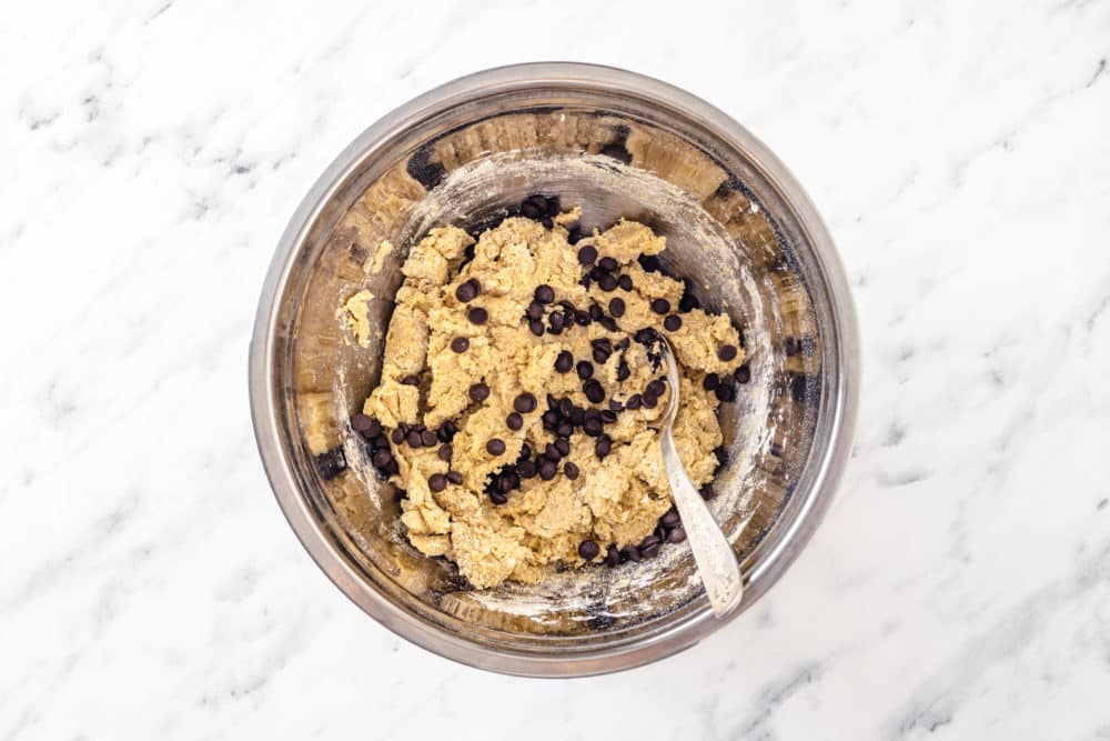 cookie dough with chocolate chips mixed in a silver bowl with a spoon.