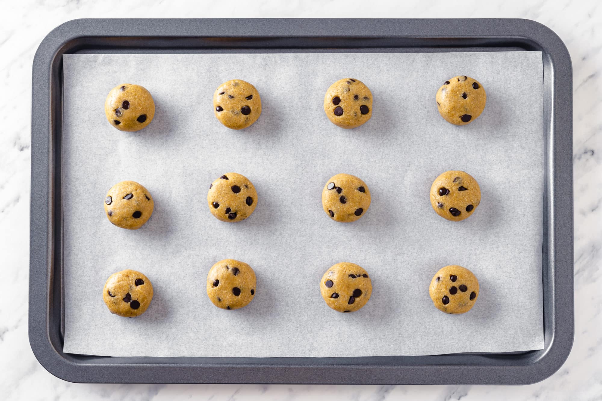 raw cookie dough scooped on top parchment paper on a baking tray.