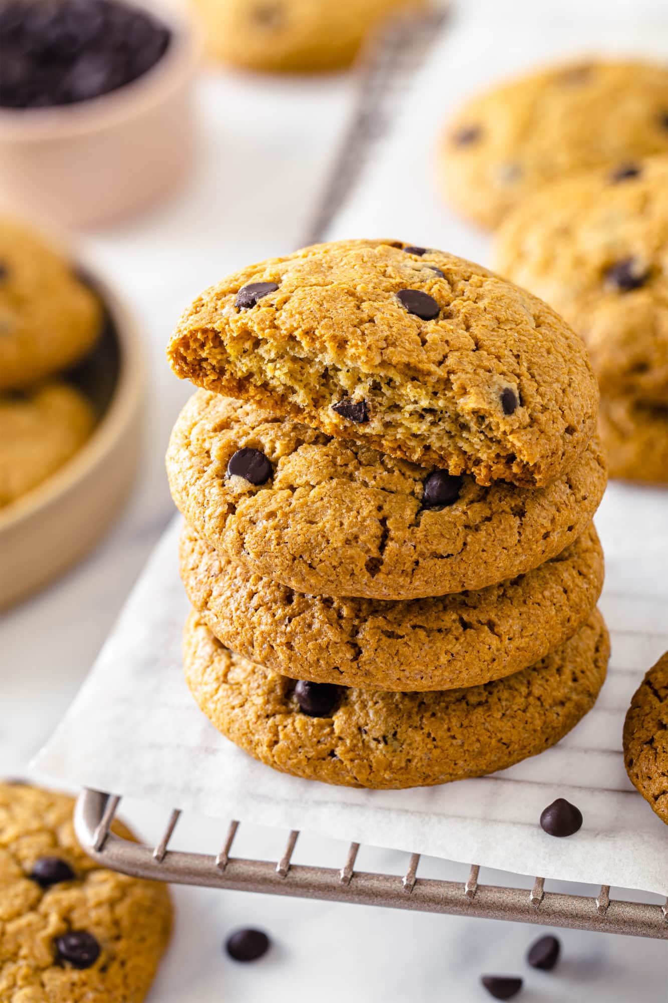 chocolate chip cookies stack with the top cookie as a half stacked on parchment paper and a cooling rack.