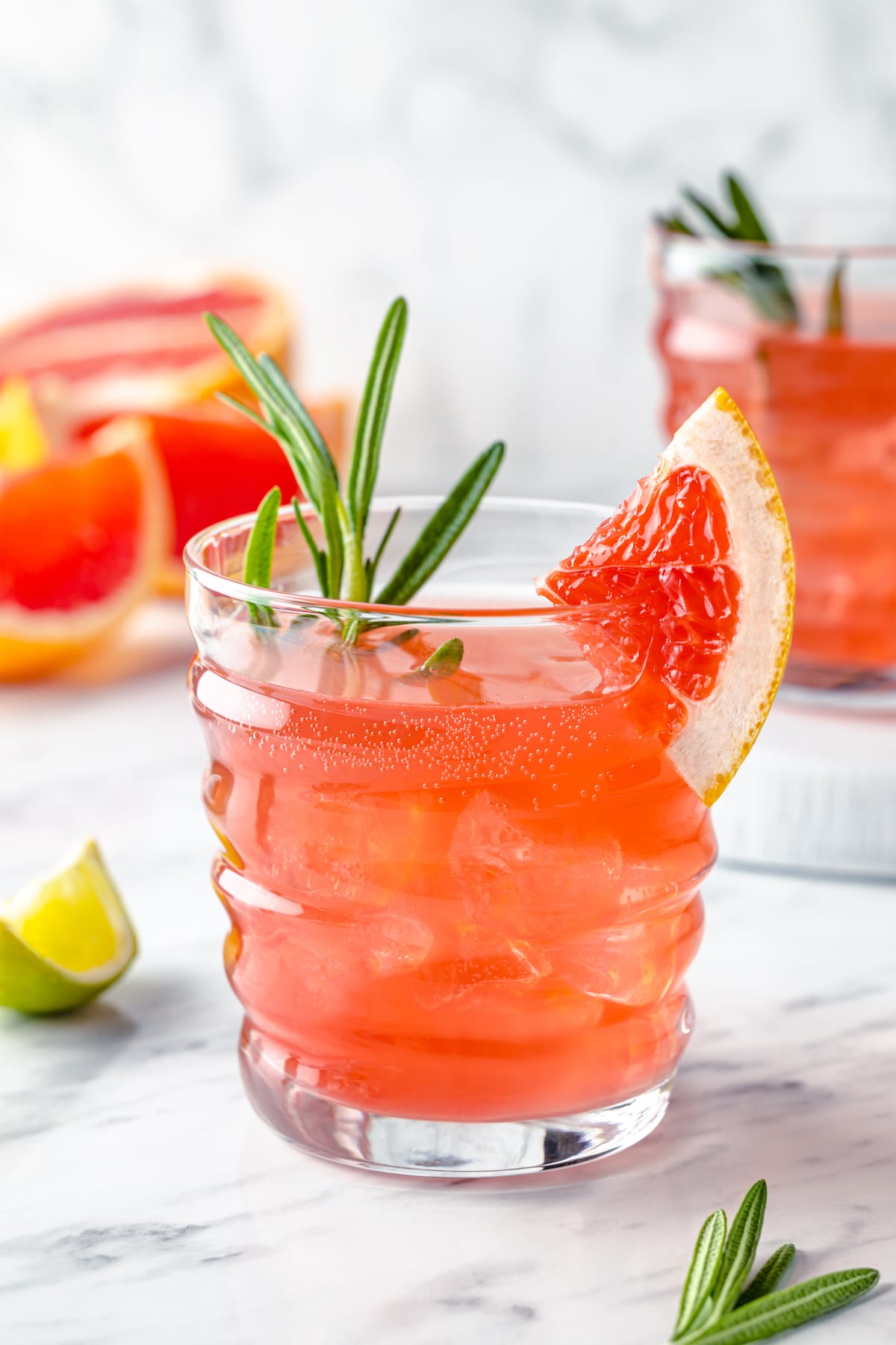 grapefruit lime drink with rosemary simple syrup in a glass cup with a sprig of rosemary and slice of grapefruit for garnish