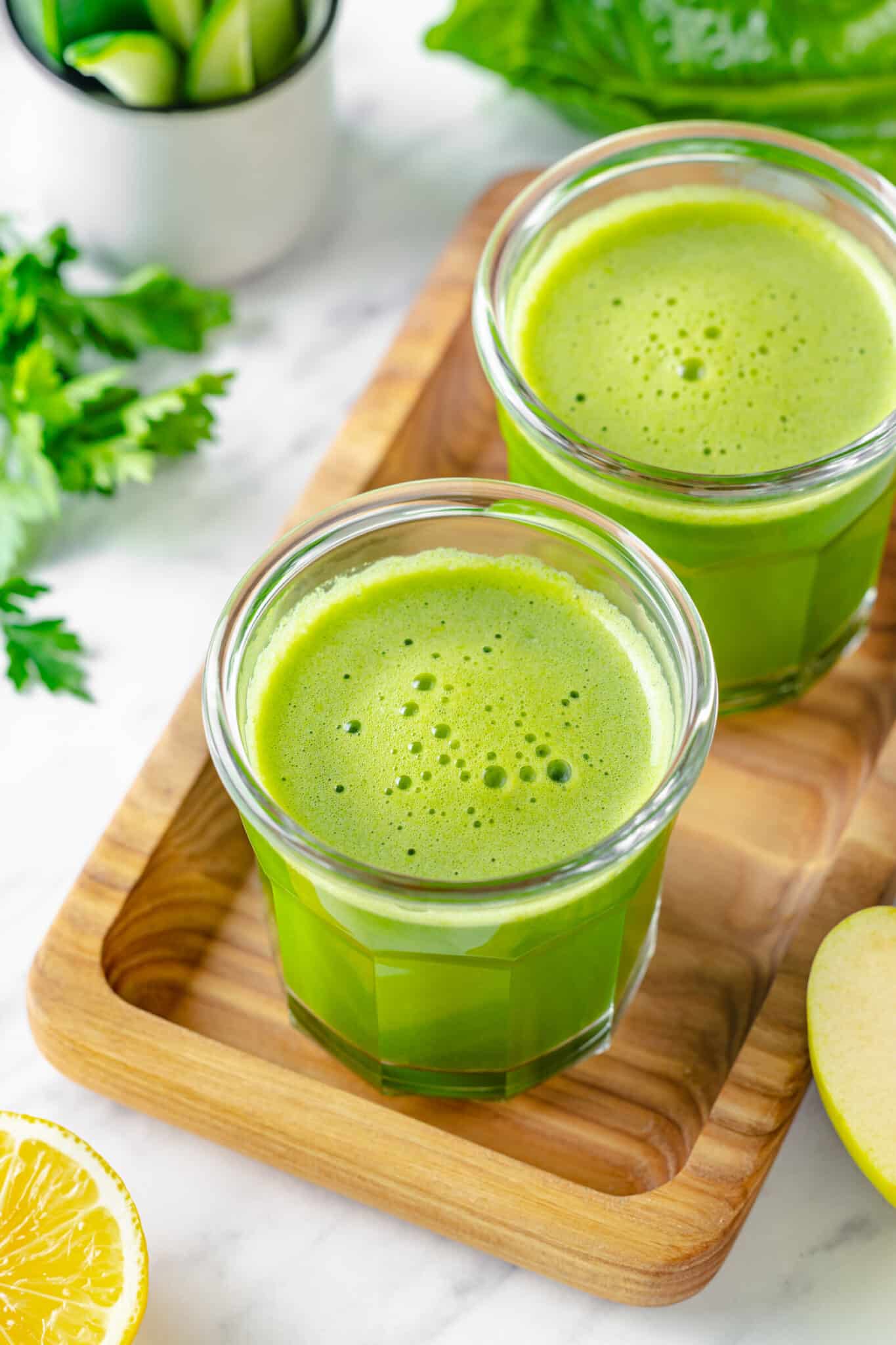 Green juice in two glasses atop a decorative tray.