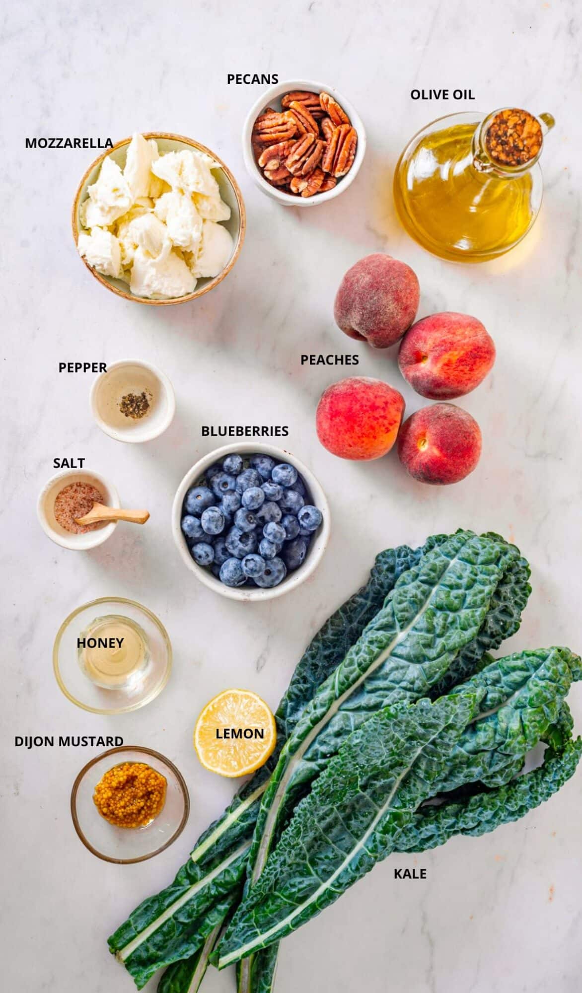 Salad ingredients spread with labels- pecans, olive oil, mozzarella, peaches, blueberries, pepper, salt, honey, lemon, kale, and dijon mustard.