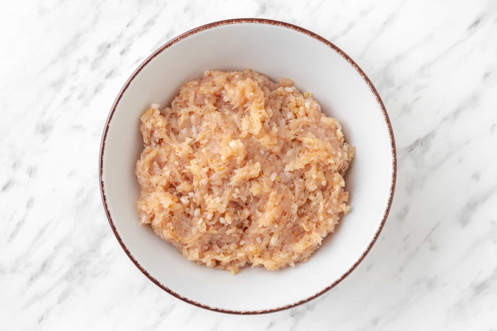 Ground chicken mixed with seasoning and rice in a bowl.