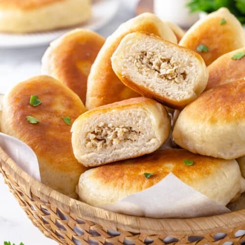 Halved piroshki atop a bowl of more piroshki.