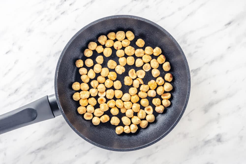 Toasting hazelnuts in a black skillet.