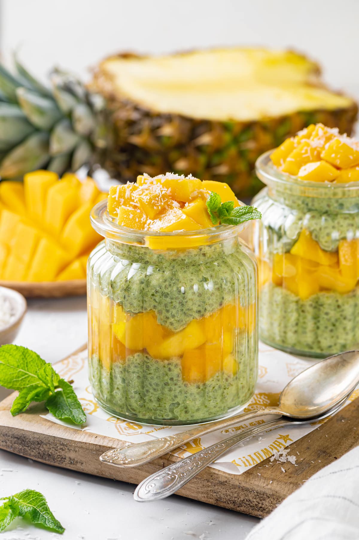 mango and spinach chia seed pudding in two jars with shredded coconut on the top, on a wooden board and parchment paper.