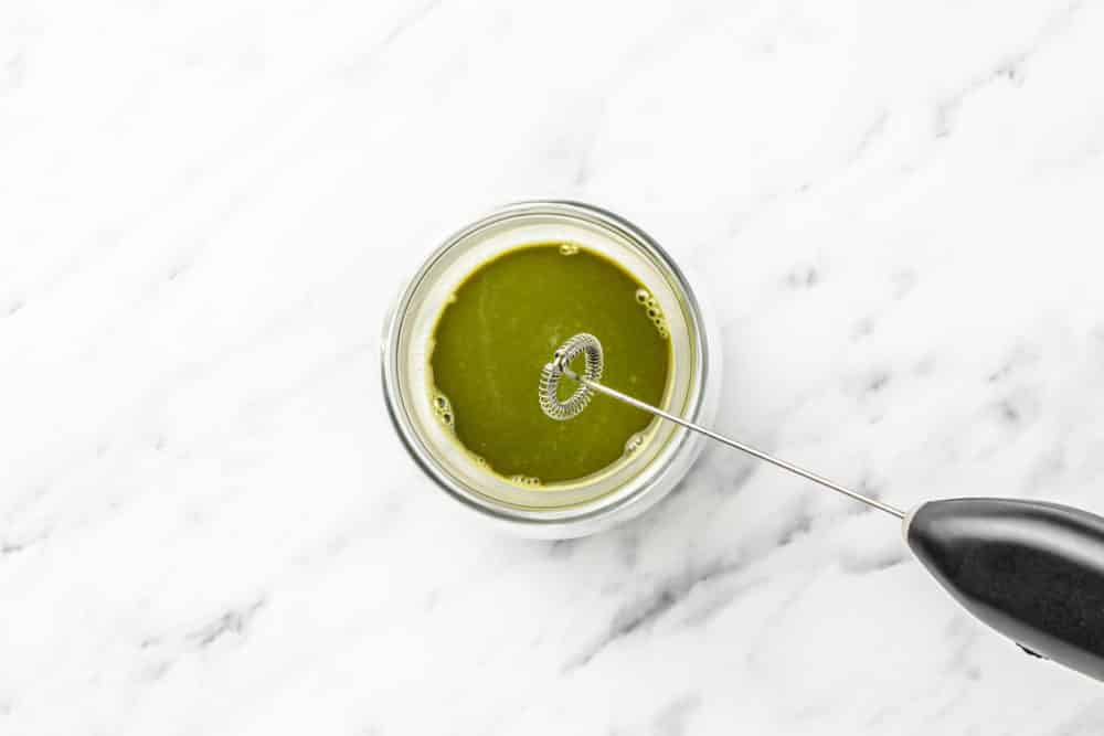 matcha and water mixed in a glass with a milk frother.