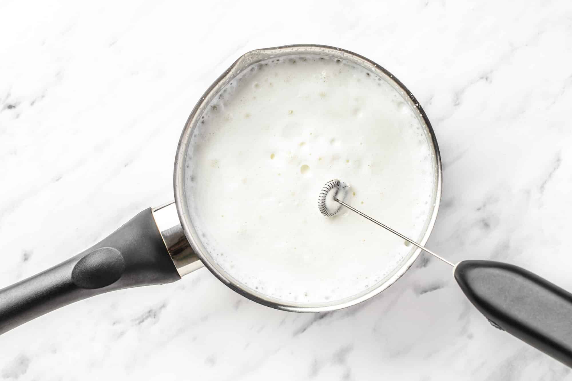 a milk frother in a saucepan with milk in it all frothed up.