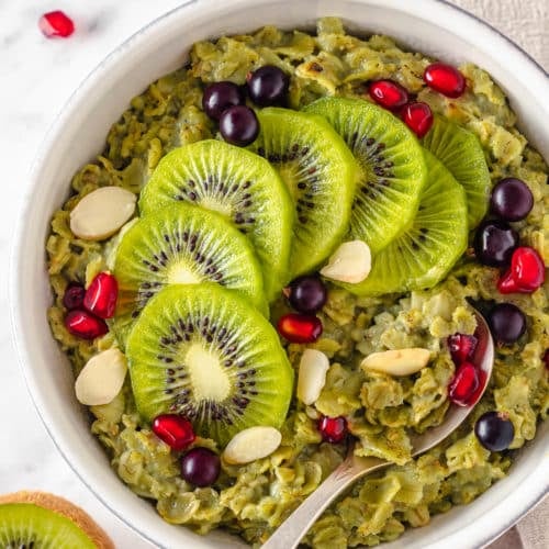 Top view of matcha oatmeal in a white bowl with sliced kiwi and almonds on top with a silver spoon.