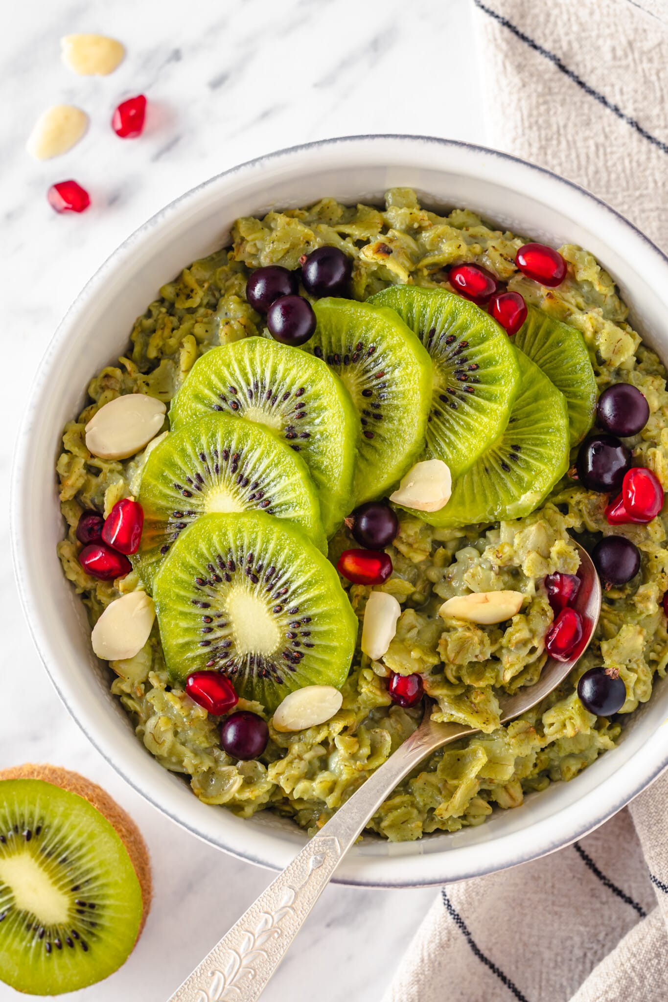 Top view of matcha oatmeal in a white bowl with sliced kiwi and almonds on top with a silver spoon.