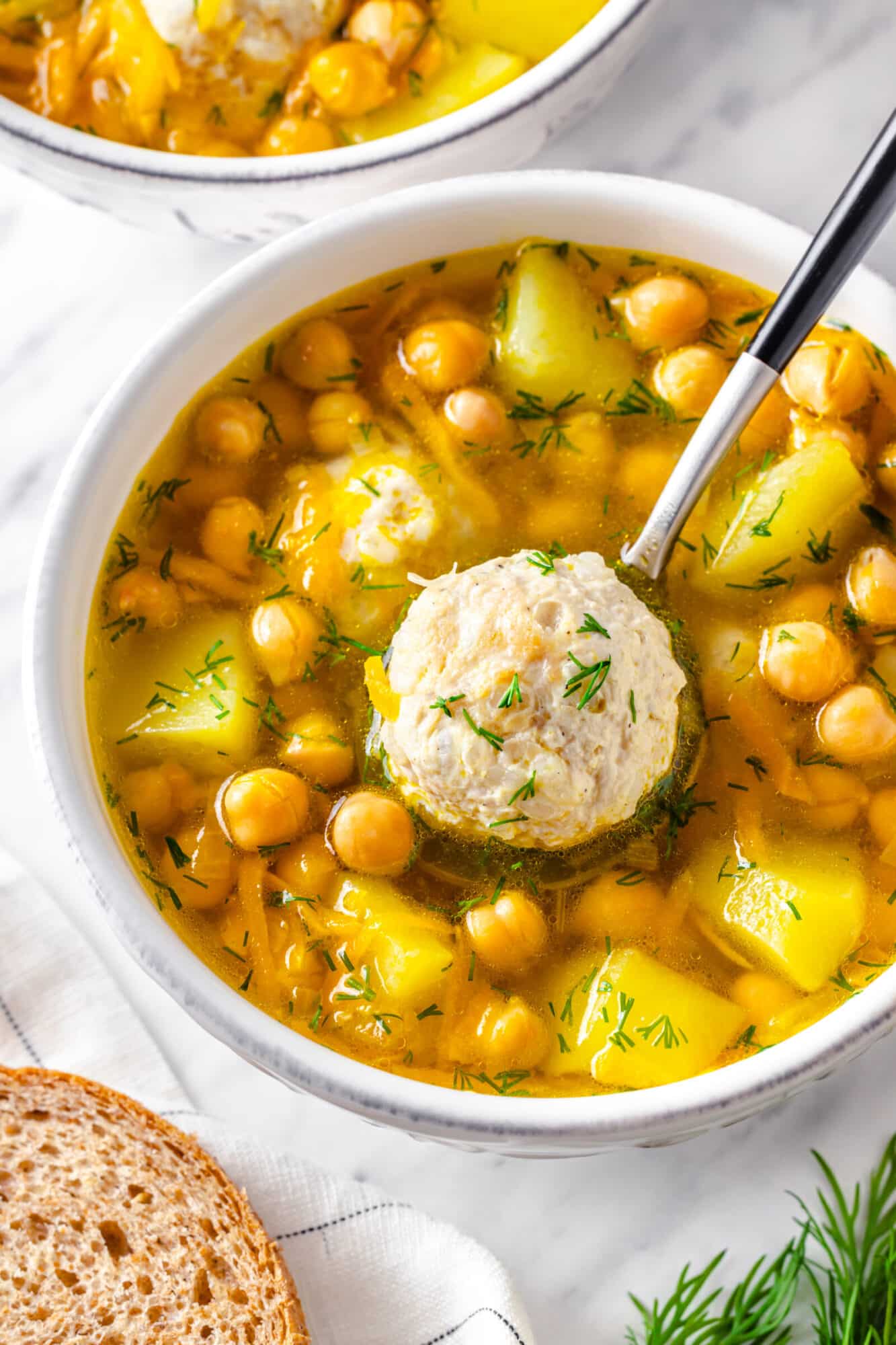 Meatball serving atop a spoon in a garbanzo bean and potato soup.