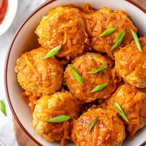 Meatballs garnished with chopped green onion in a bowl.