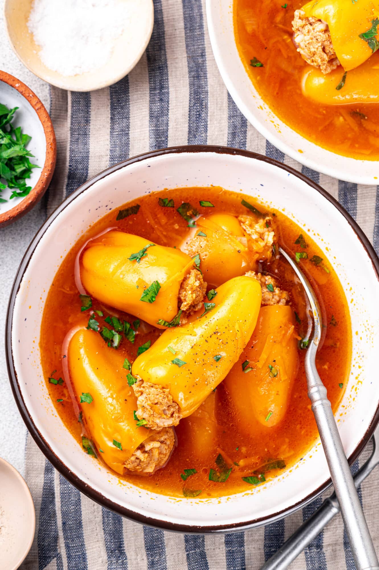 Mini stuffed peppers in a bowl serving with a spoon on the side and garnished with parsley on top.