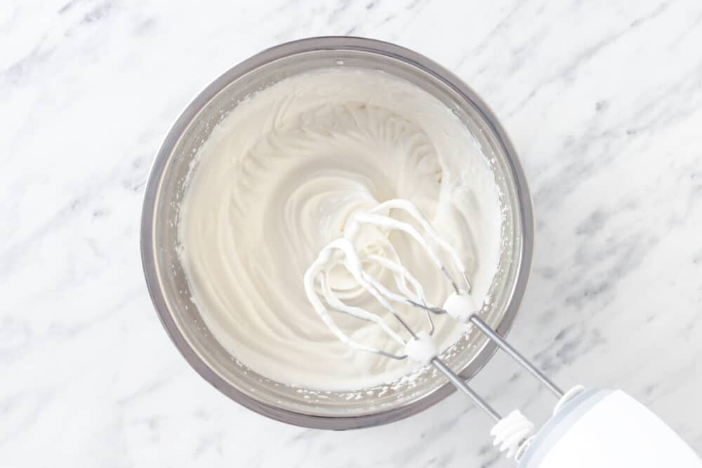 Mixed cream and powdered sugar in a silver mixing bowl with mixers.