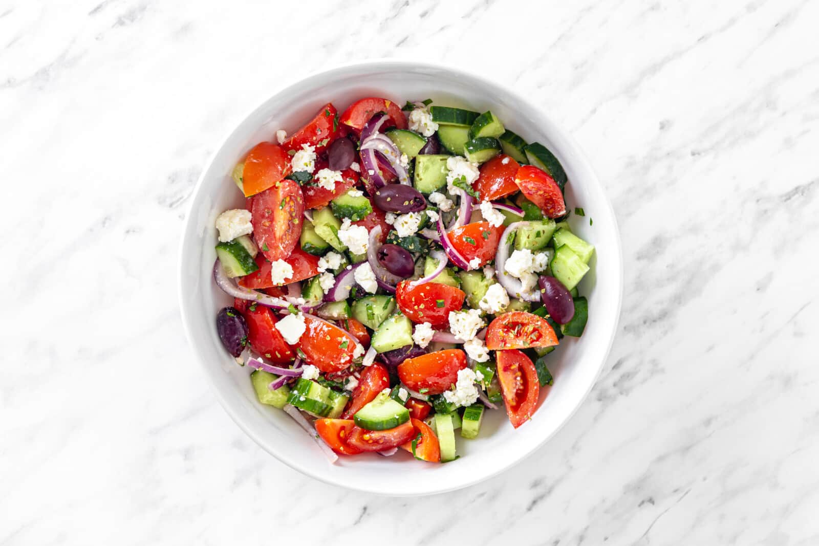 Greek salad mixed in a white bowl.