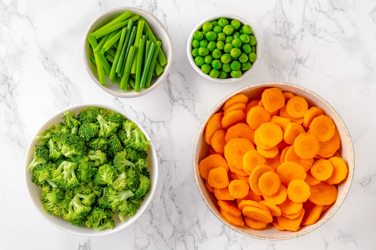 broccoli florets, sliced carrots, green peas, and green onion in individual bowls.